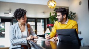 A woman and a man smiling at a hotel check-in counter, with paperwork and a computer.